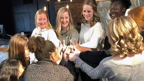 Group of girls together with hands in the center of a circle and their thumbs up